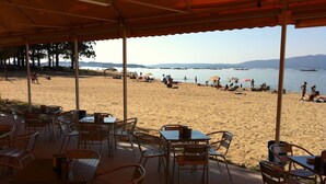A beachside cafe with outdoor seating overlooking a sandy beach and the sea.
