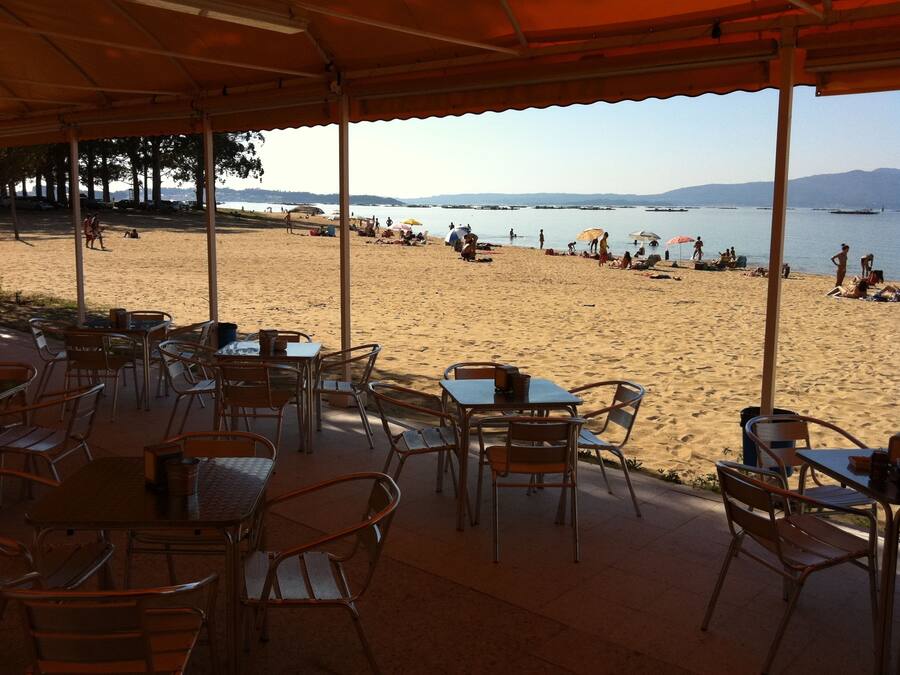 A beachside cafe with outdoor seating overlooking a sandy beach and the sea.