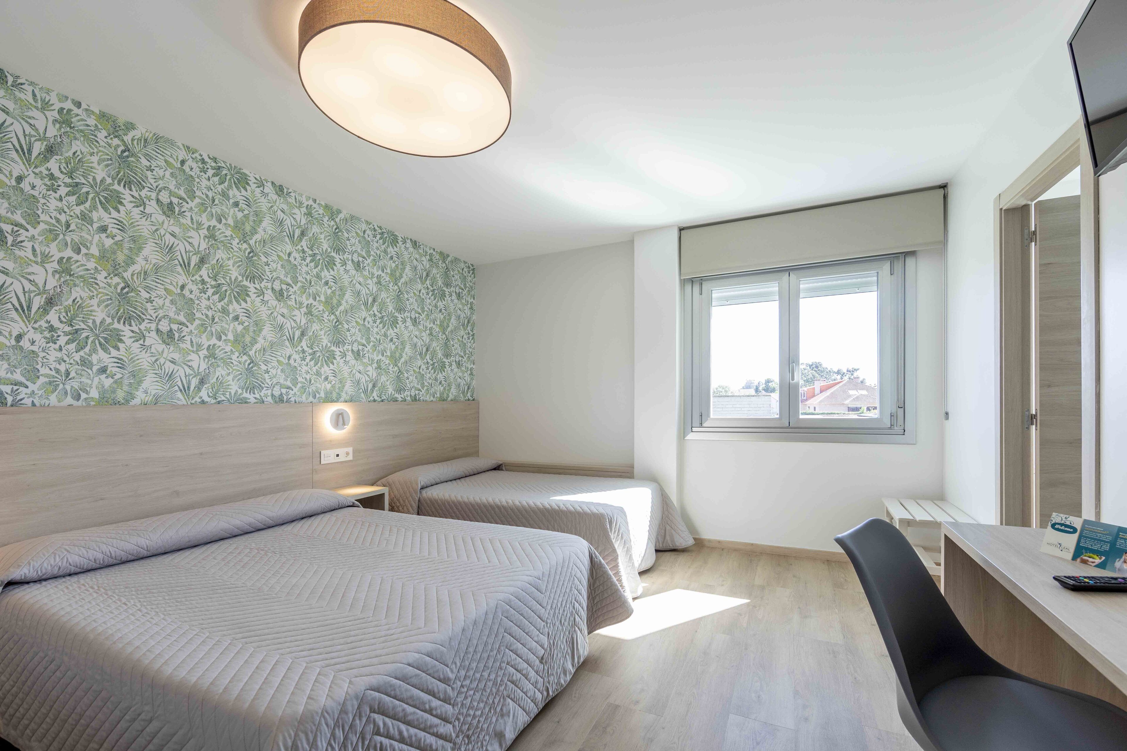 Habitación de hotel moderna con dos camas, un escritorio y un ventanal grande.