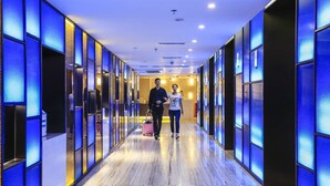 Un pasillo de hotel con diseño moderno, que presenta piso de madera y paneles azules iluminados en las paredes.