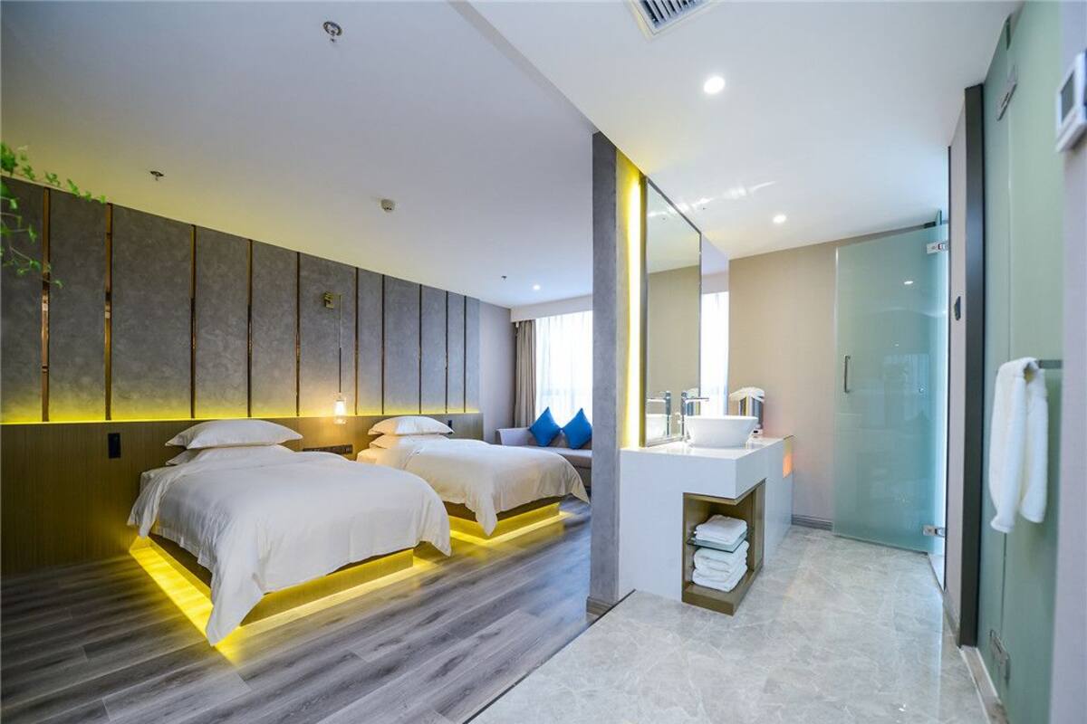 A modern hotel room with a large bed, a separate seating area, a bathroom with a glass shower, and a minimalist design.