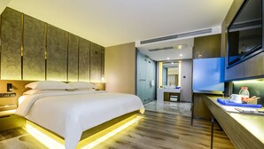 Una habitación de hotel moderna con una cama grande, un escritorio con televisor de pantalla plana y un baño visible a través de una puerta abierta.
