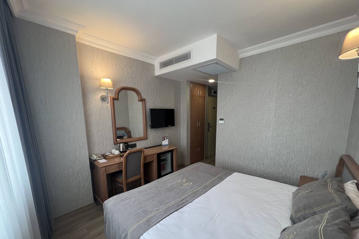 Ein Hotelzimmer mit einem Bett, einem Schreibtisch mit Stuhl, einem Fernseher und einem Kleiderschrank.