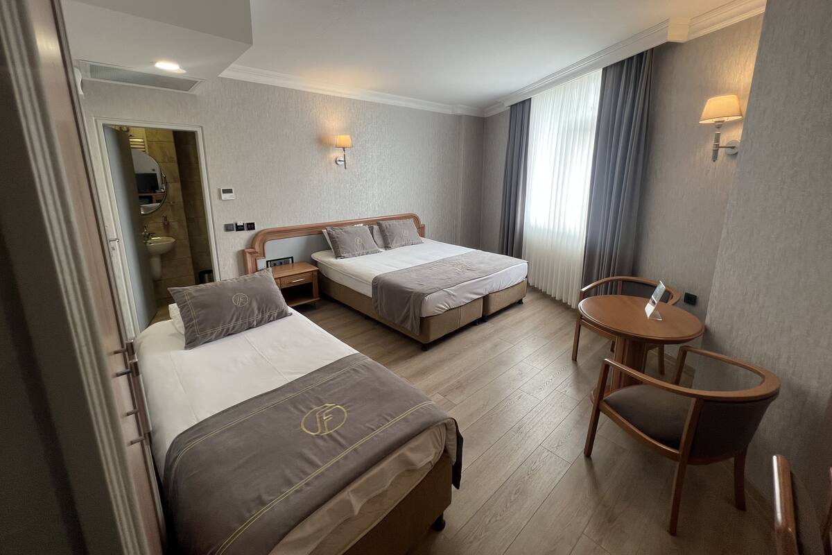 Ein Hotelzimmer mit zwei Betten, einem kleinen Tisch und einem Stuhl. Ein Badezimmer ist durch eine geöffnete Tür erkennbar.