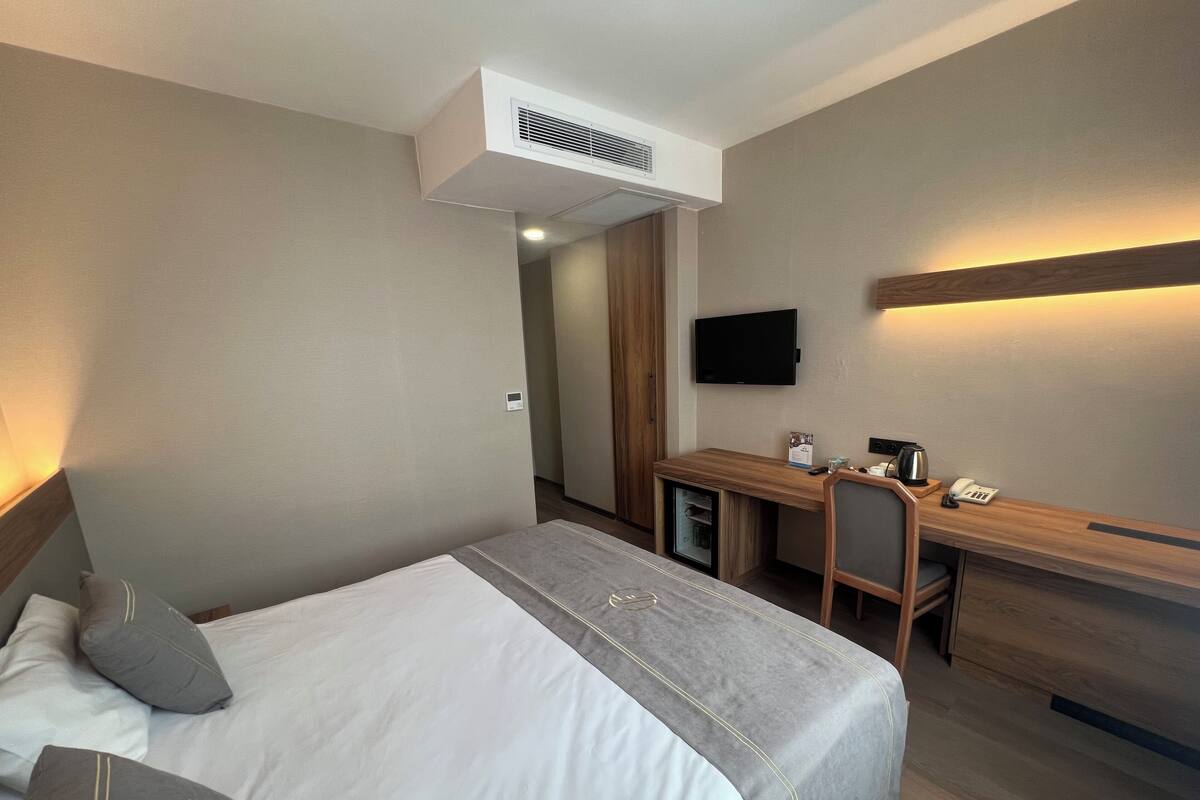 Ein Hotelzimmer mit einem Bett, einem Schreibtisch, einem Sessel, einem Fernseher und einer Minibar.