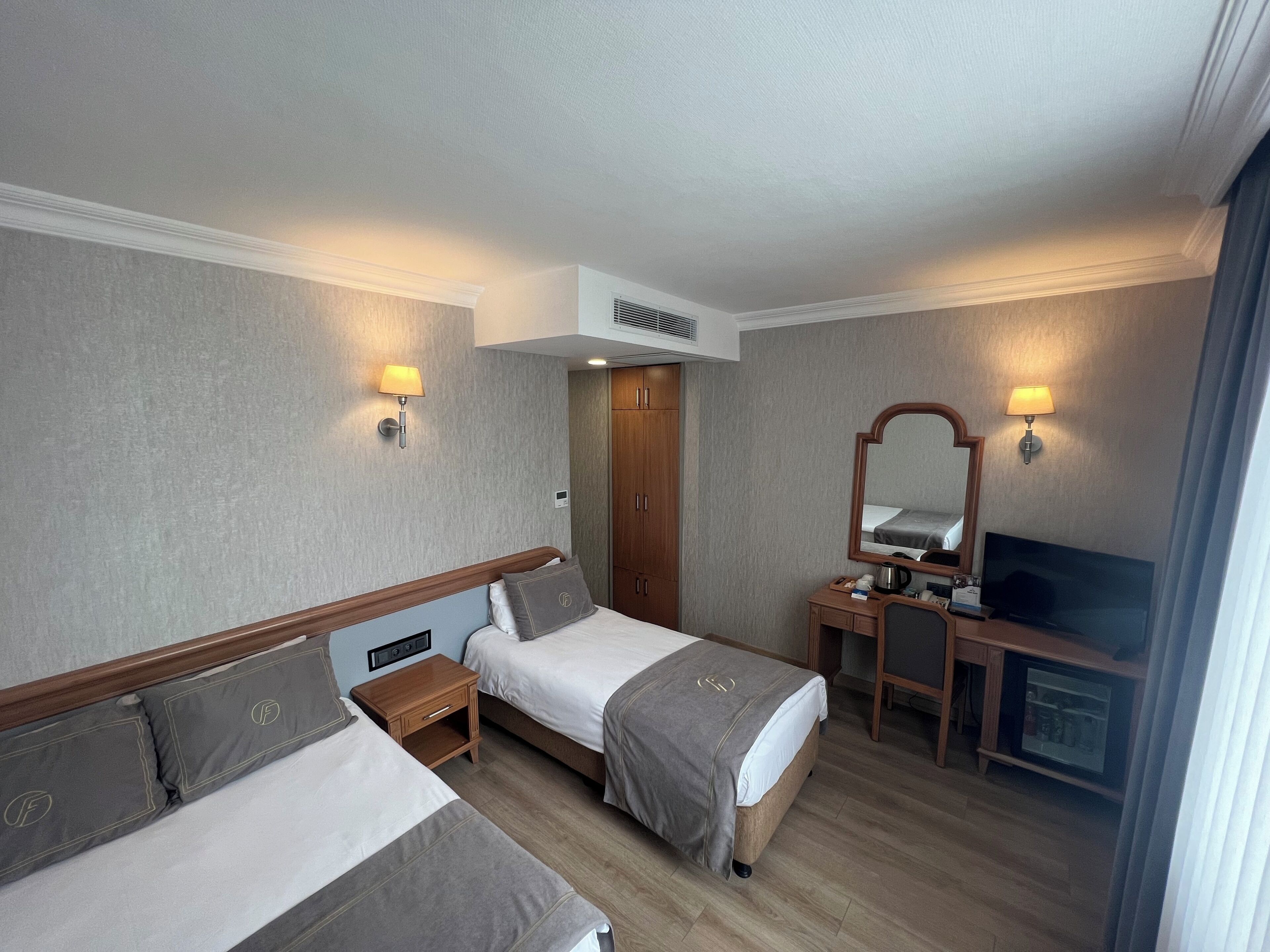 Una habitación de hotel con dos camas, un escritorio con espejo, televisión y armario.
