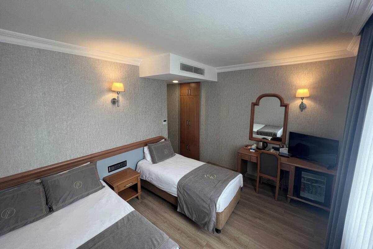 Una habitación de hotel con dos camas, un escritorio con espejo, televisión y armario.