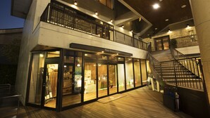 A modern hotel with a glass facade, a wooden deck, and a staircase connecting the levels. - Villa Terrace Omura Hotels & Resorts (Omura)