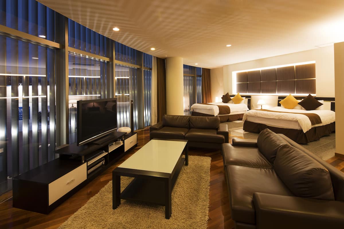A modern hotel room with a large TV, a sofa, a bed, and a desk.