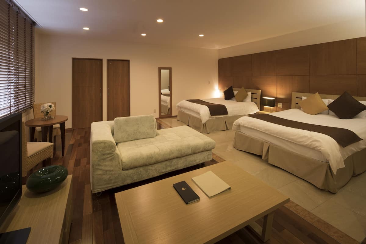 A hotel room with two beds, a sofa, a small table, and a mirror.