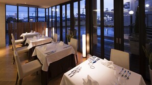 A restaurant with multiple tables set for dining, large windows offering a view of the outside, and a wooden floor. - Villa Terrace Omura Hotels & Resorts (Omura)