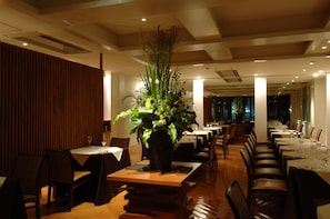A restaurant with multiple tables and chairs, a central floral arrangement, and a wooden panel wall. - Villa Terrace Omura Hotels & Resorts (Omura)