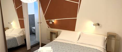 A modern hotel room with a large bed, bedside tables, a mirror, and a view of the bathroom.