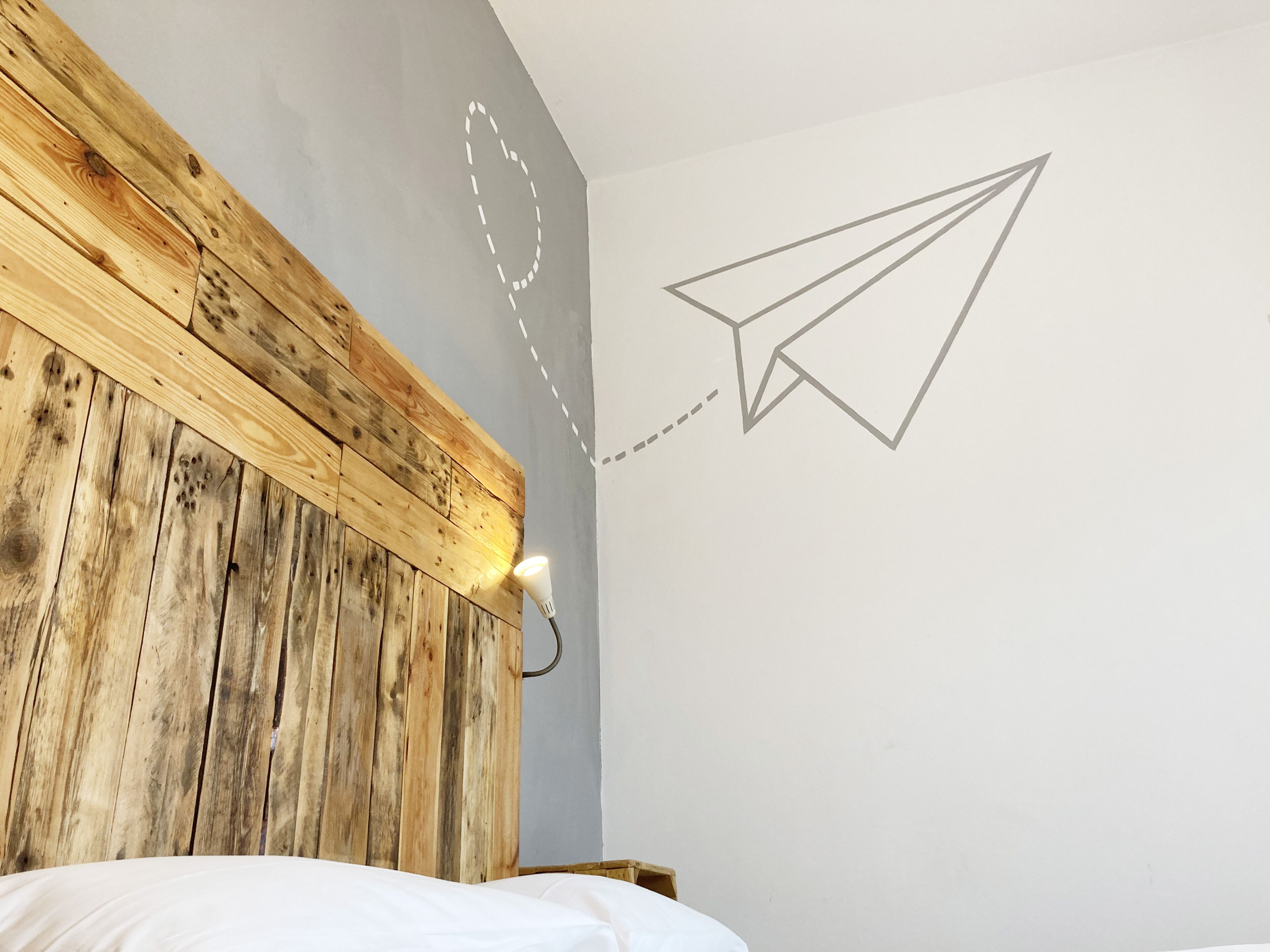 Une chambre avec une tête de lit en bois, un mur blanc et un dessin d’avion en papier.