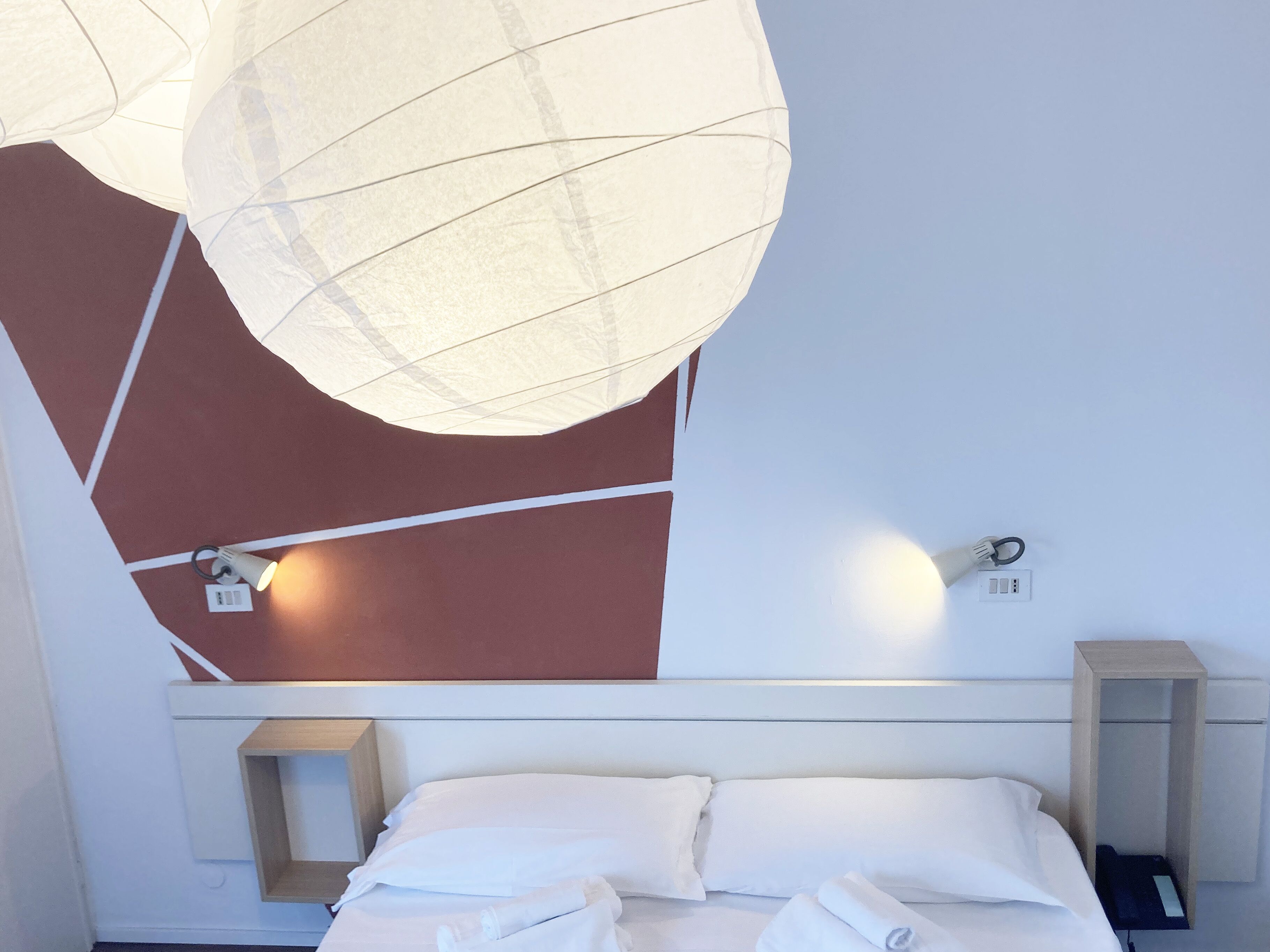 A modern hotel room with a bed, bedside table, and a wall-mounted lamp.