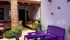An outdoor patio area with a purple table and chairs, a stone pillar, and a balcony with plants. - Lusin Butik Hotel (Ayvalik)