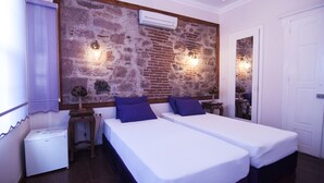 A room with two single beds, a brick wall, an air conditioning unit, a small table, and a mirror. - Lusin Butik Hotel (Ayvalik)