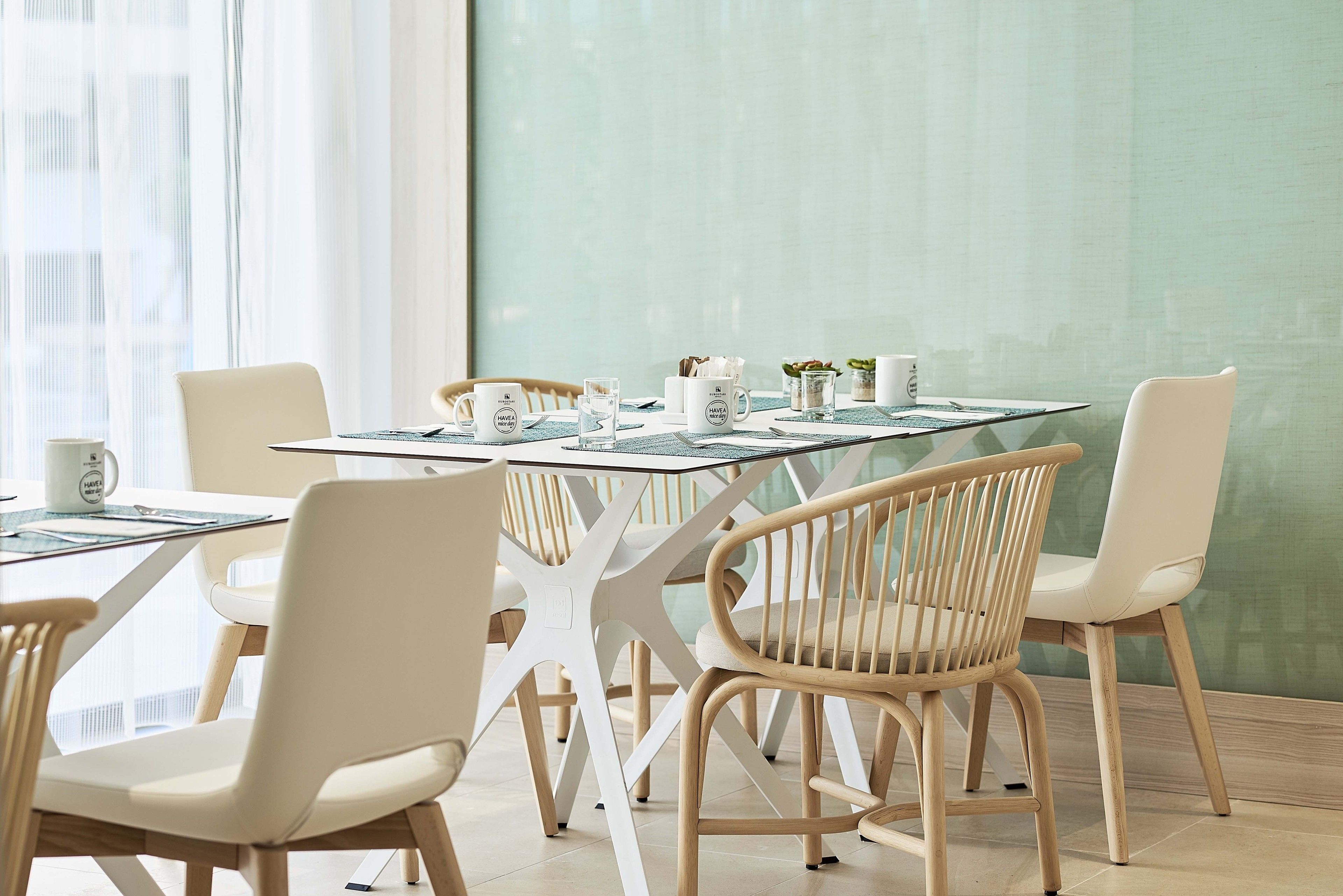 A modern dining area with a glass-top table, white chairs, and a green wall.