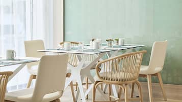 A modern dining area with a glass-top table, white chairs, and a green wall.