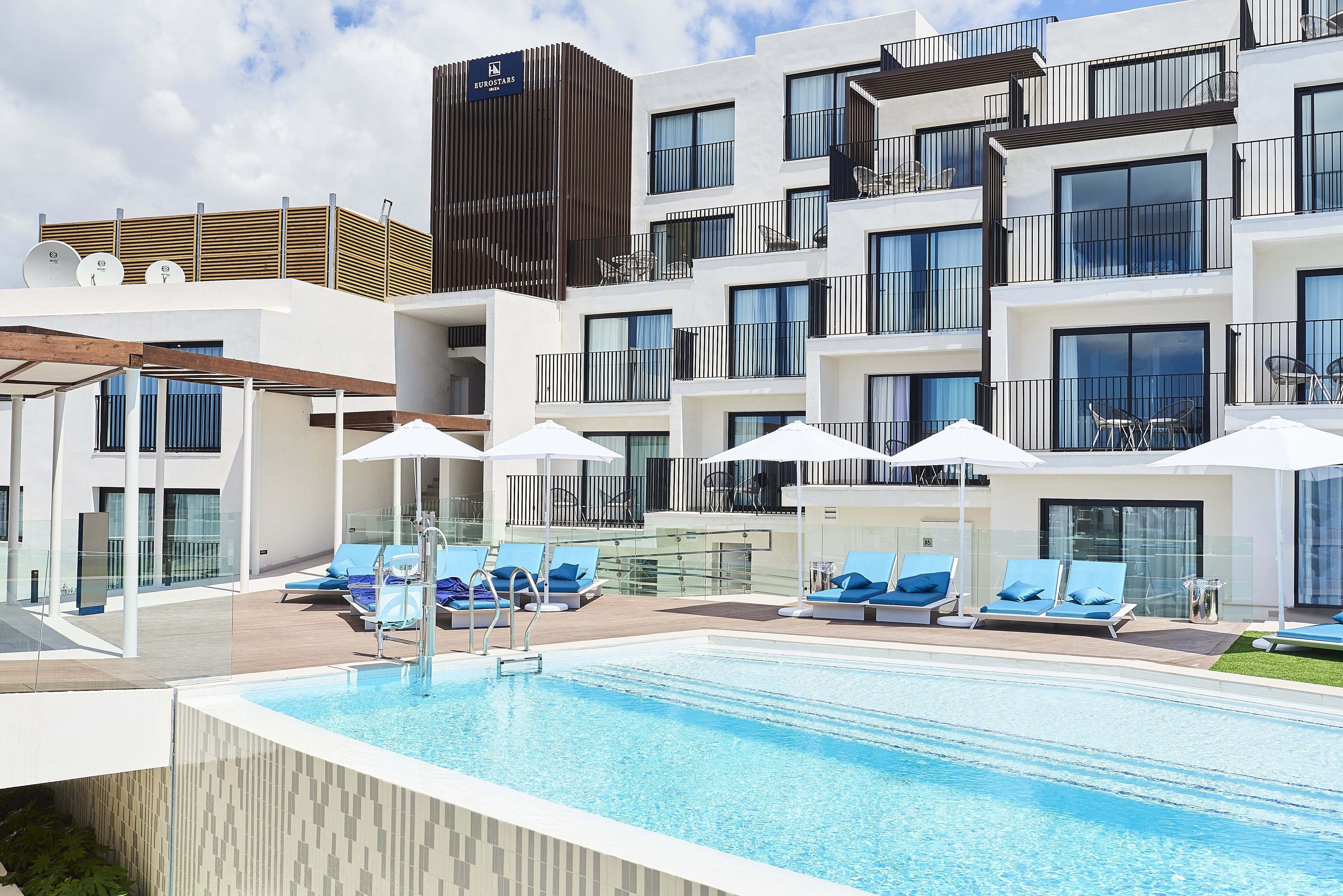 Un hotel moderno con piscina en la azotea, tumbonas y vistas al horizonte de la ciudad.