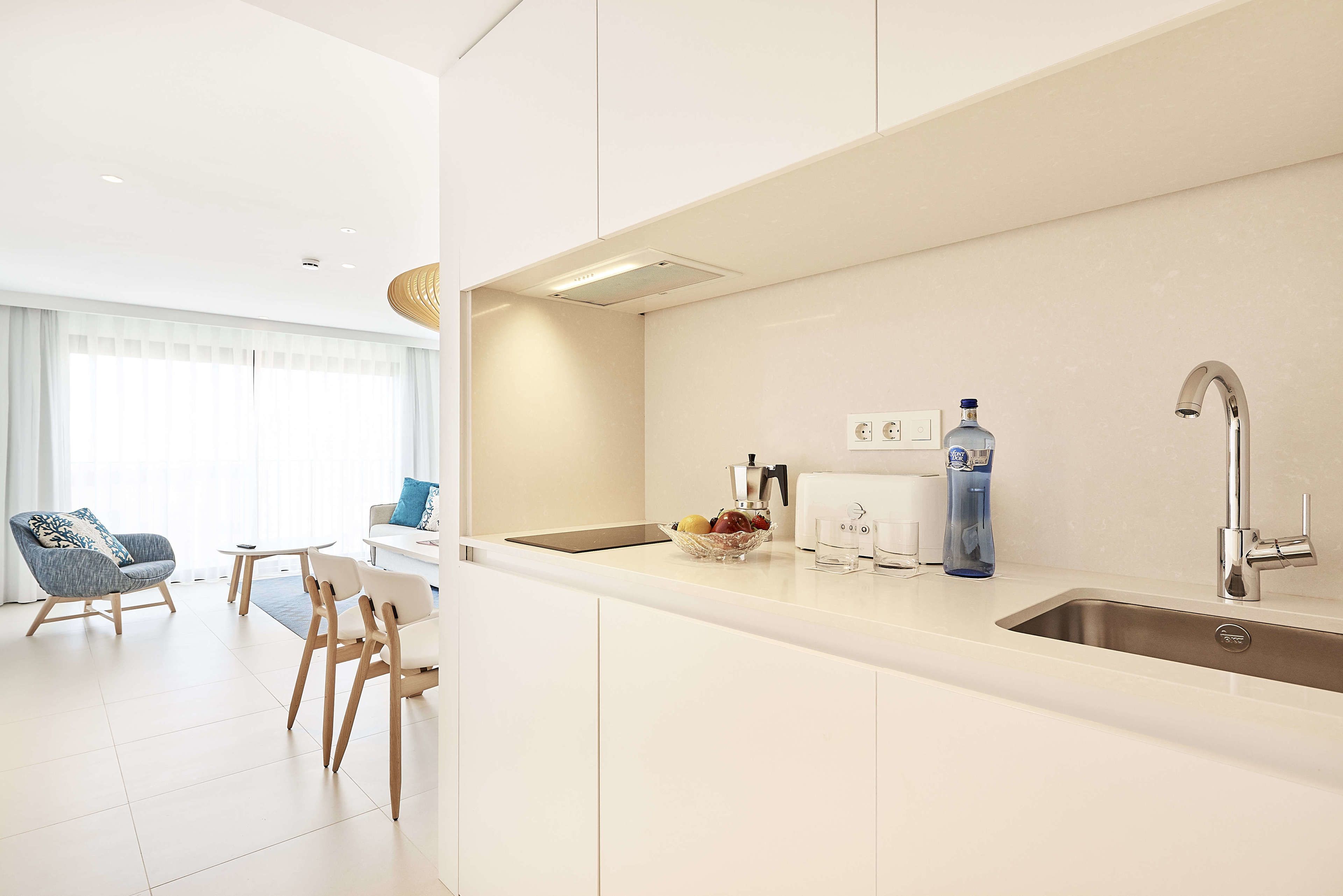 A modern kitchen with white cabinetry, a stainless steel sink, and a fruit bowl on the counter.