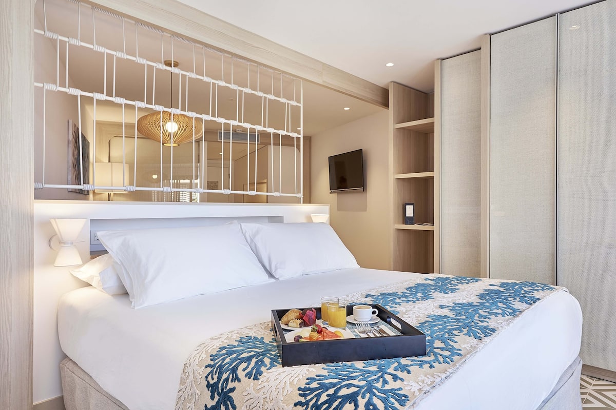Een hotelkamer met een net opgemaakt bed, een dienblad met ontbijtartikelen en een televisie aan de muur.