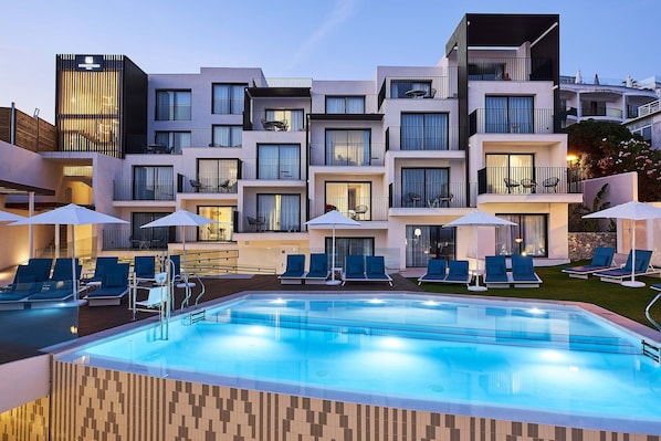Un hotel moderno con piscina, asientos exteriores y balcones.