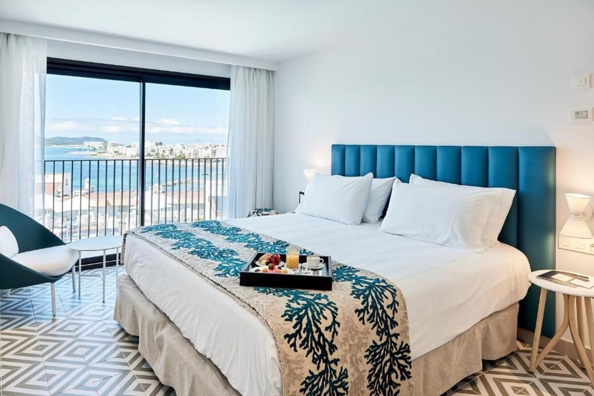 Une chambre d’hôtel avec un grand lit, une vue sur la plage et un plateau de petit-déjeuner posé sur le lit.