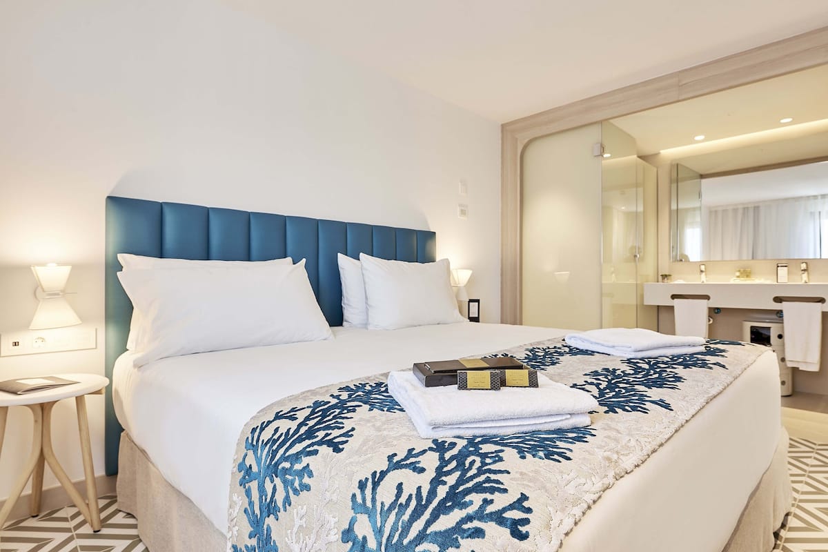 Hotelkamer met een groot bed, nachtkastje, badkamer met spiegel en handdoekrek.