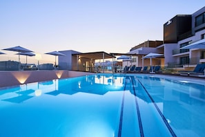 Una piscina en la azotea con sillones de descanso y sombrillas, rodeada de edificios modernos.