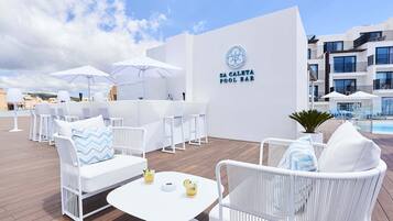 An outdoor seating area with white wicker furniture, umbrellas, and a pool bar sign.