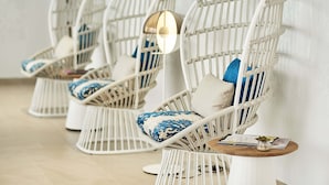 A row of white wicker chairs with blue and beige cushions, a round wooden table with a lamp, and a magazine on the table. - Eurostars Ibiza (Ibiza Town)