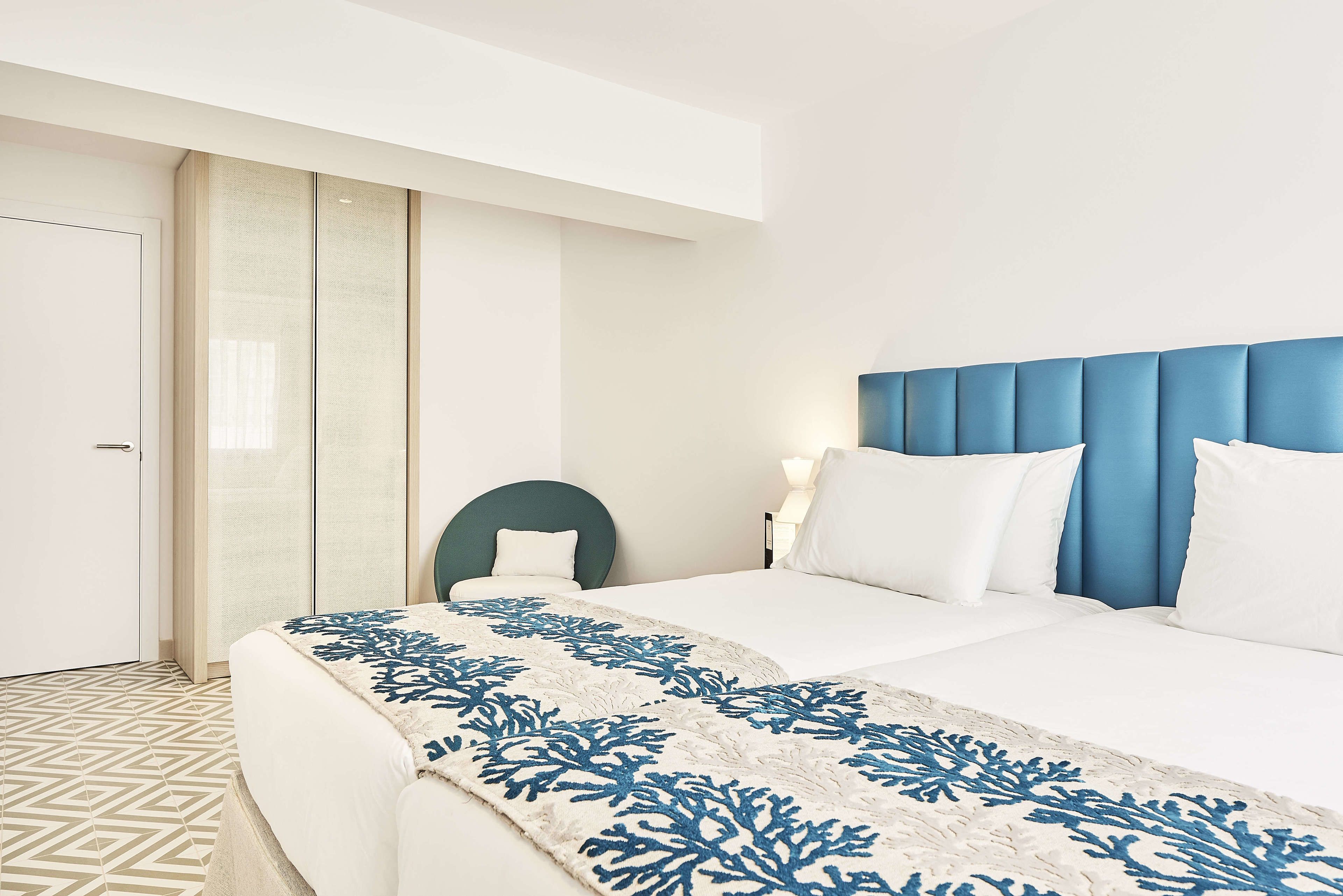 Une chambre d’hôtel avec un lit, une chaise et une table de chevet avec une lampe.