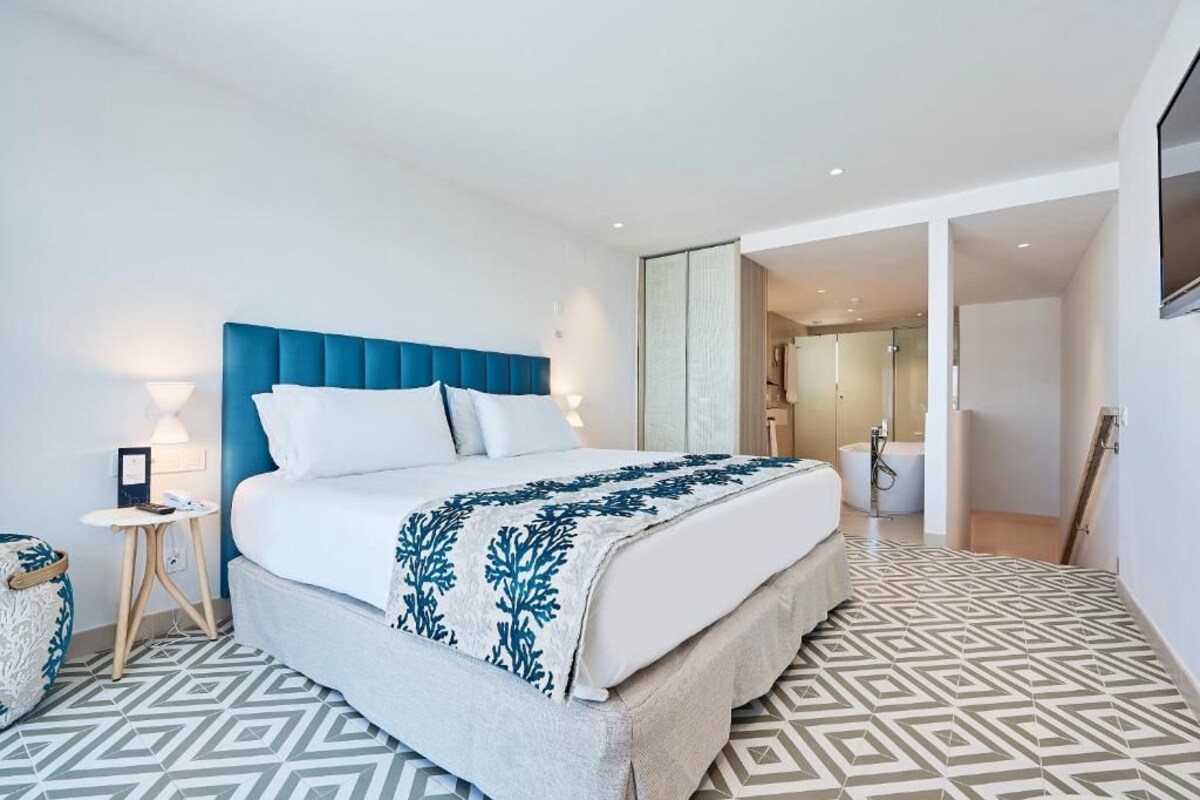 A modern hotel room with a large bed, a blue headboard, and a patterned floor.