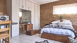A bedroom with a brick wall, a bed with multiple pillows, a wooden nightstand, and a TV on a cabinet. - 800 at Merton (Pretoria)