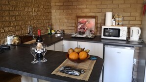 A compact kitchen with a brick wall, a microwave, a coffee maker, and a bowl of oranges on the counter. - 800 at Merton (Pretoria)