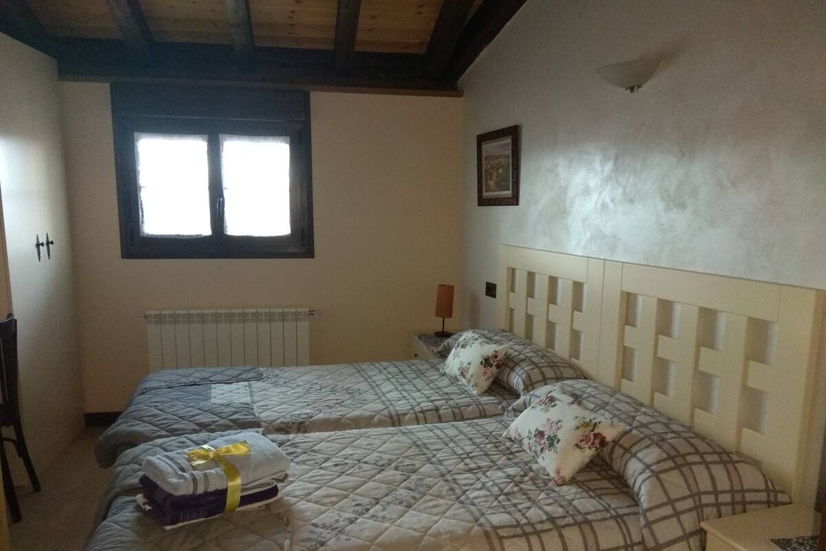 Ein Zimmer mit zwei Betten, einem Fenster, einem Heizkörper und einem gerahmten Bild an der Wand.