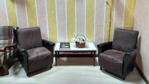 A room with striped wallpaper, two leather chairs, a small table with a book and a basket of flowers, and a floor lamp. - La Cerca de Doña Jimena (Ibeas de Juarros)