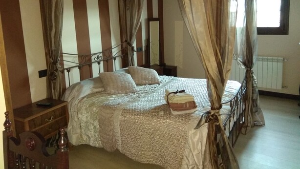 A four-poster bed with a canopy, a wooden nightstand, and a dresser with a mirror. - La Cerca de Doña Jimena (Ibeas de Juarros)