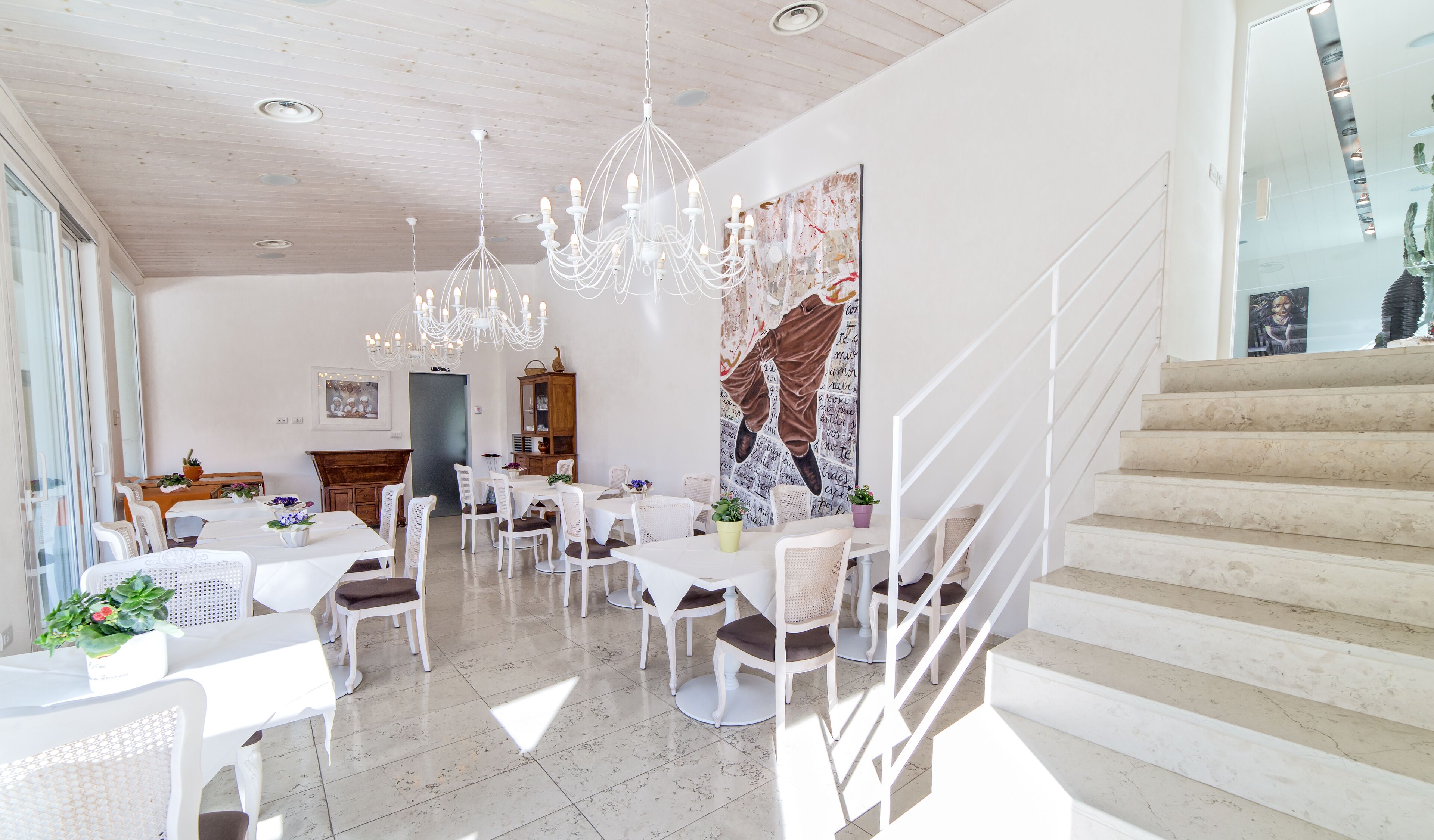A spacious dining area with white furniture, a chandelier, and a staircase.
