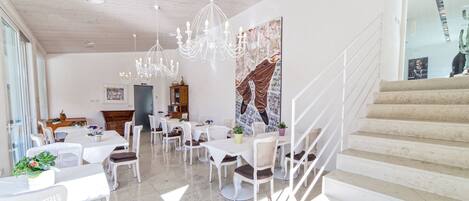 A spacious dining area with white furniture, a chandelier, and a staircase.