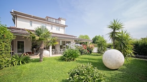 A two-story house with a covered patio area, surrounded by well-maintained lawns and various plants. - Hotel Radice (Civitanova Marche)