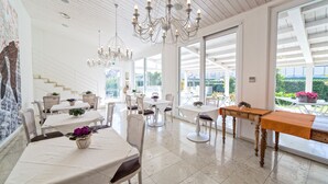 A bright, spacious dining area with white furniture, large windows, and a chandelier. - Hotel Radice (Civitanova Marche)