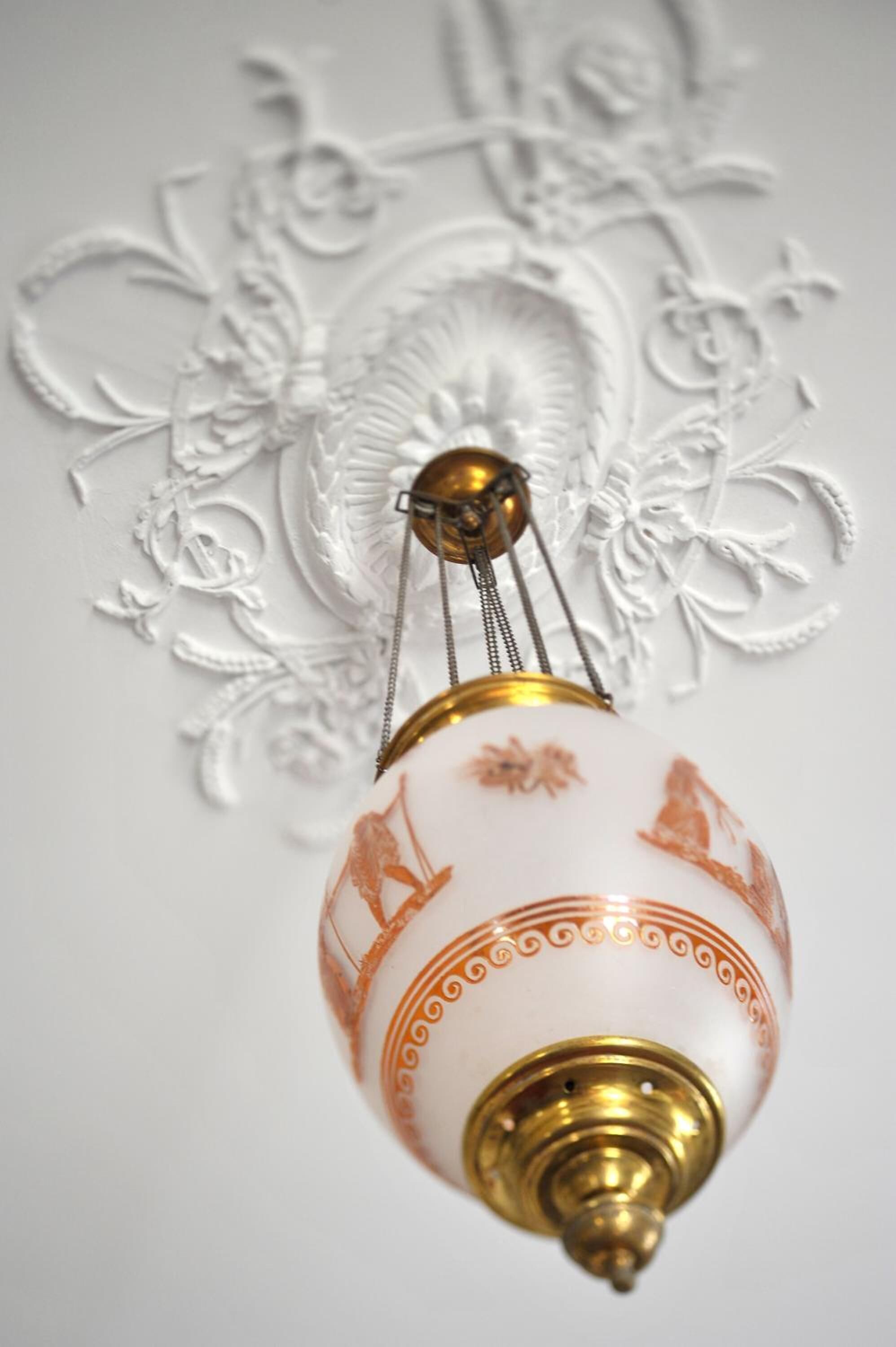 A hanging light fixture with a white and orange design, featuring a central brass element and decorative patterns.
