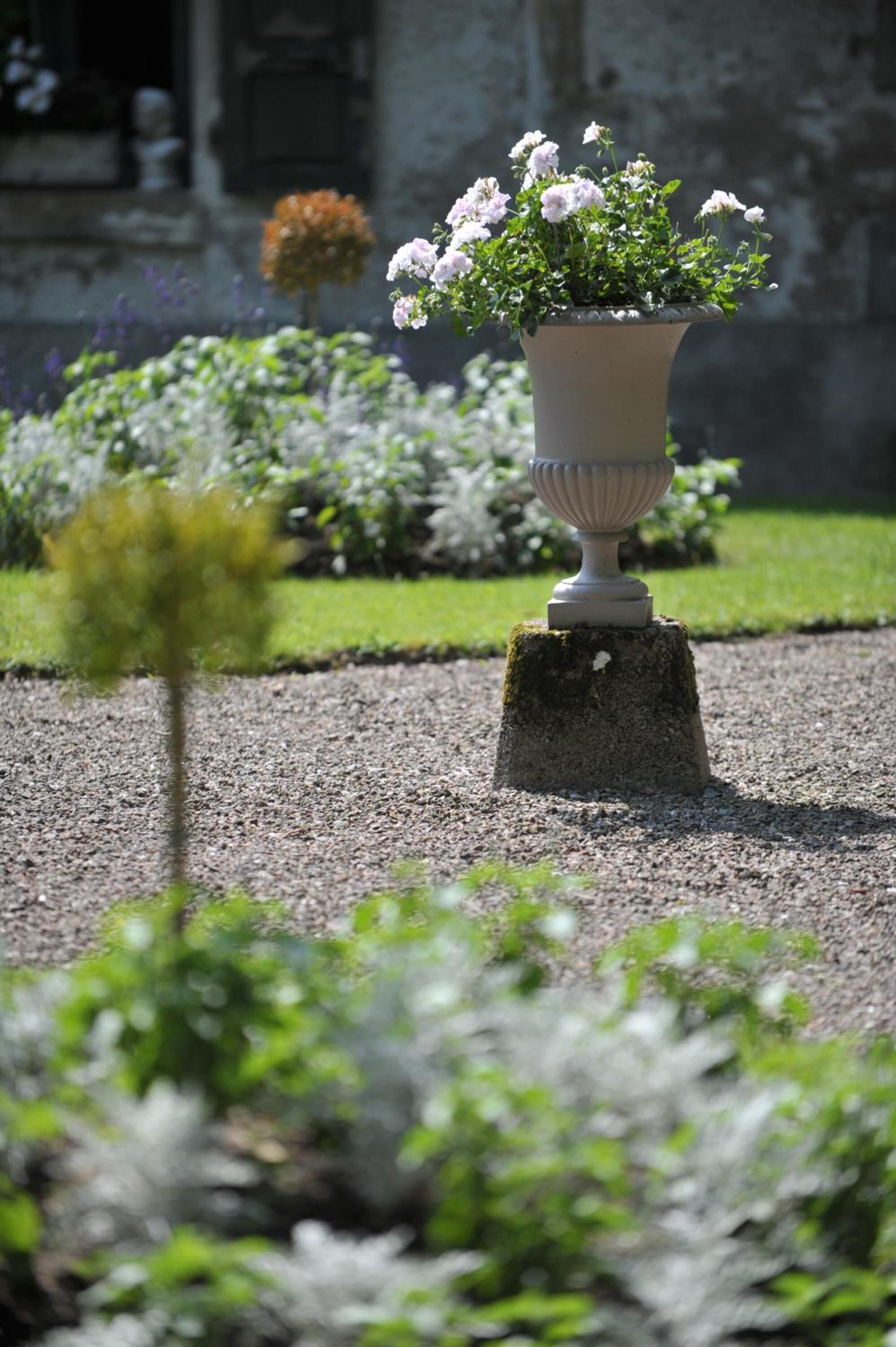 Un jardín con una jardinera grande y ornamentada llena de flores, ubicada sobre un tocón cubierto de musgo.