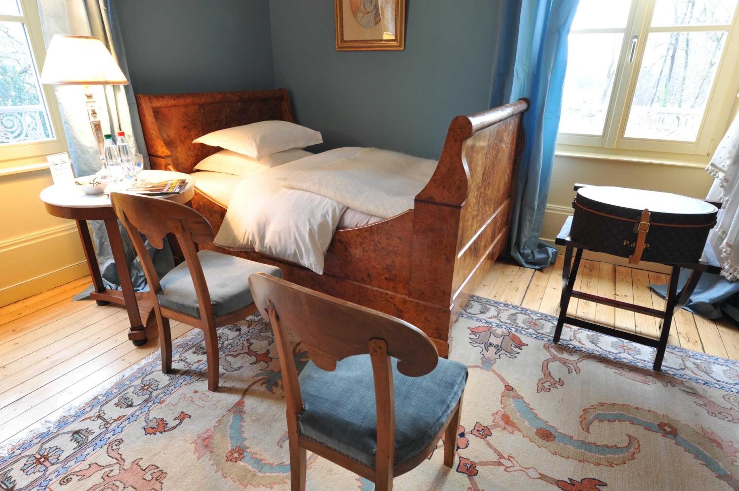 A neatly arranged bedroom with a wooden bed, a small round table with a lamp, a chair, and a rug.
