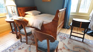 A neatly arranged bedroom with a wooden bed, a small round table with a lamp, a chair, and a rug.
