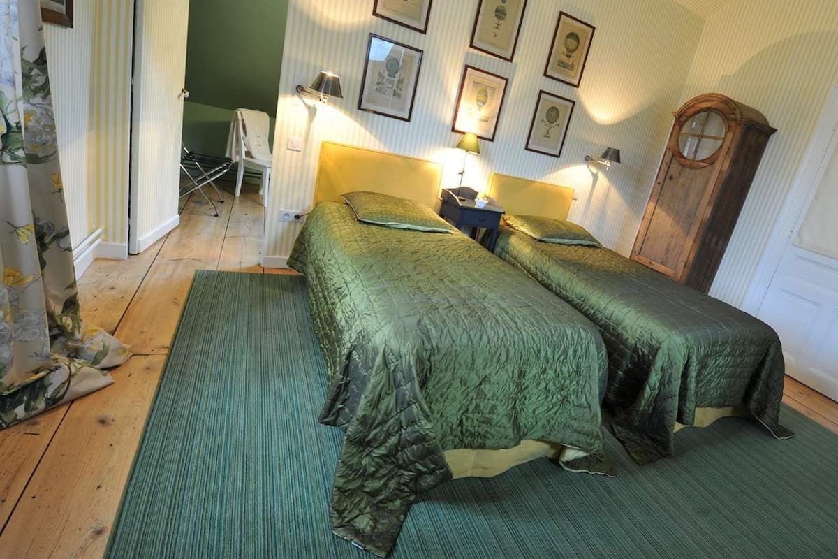 A bedroom with two beds, a wooden wardrobe, and a wall with framed pictures.