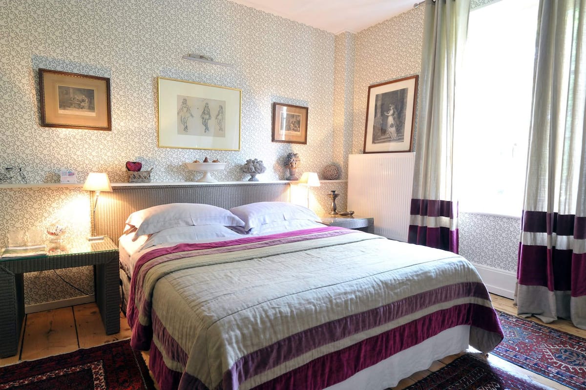 A neatly arranged bedroom with a bed, two bedside tables, a dresser, and framed pictures on the wall.