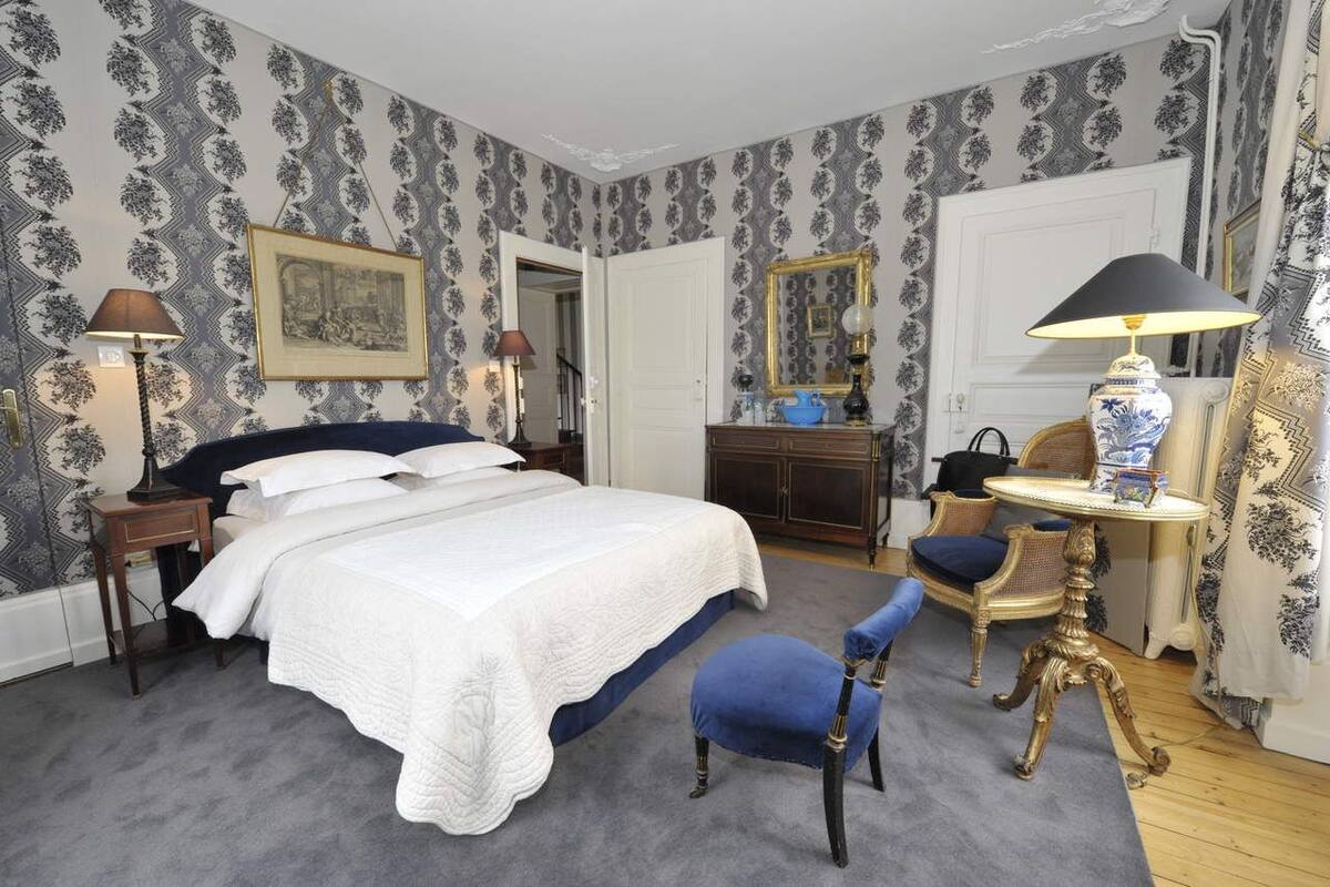 A bedroom with a large bed, a dresser, a chair, a table, and a mirror.
